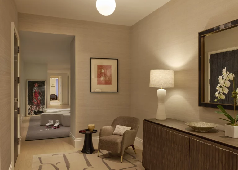 Entry gallery in a Snøhetta Upper West Side residence featuring a sculpted wood console, mirror, and art wall, leading into the interconnected rooms beyond.