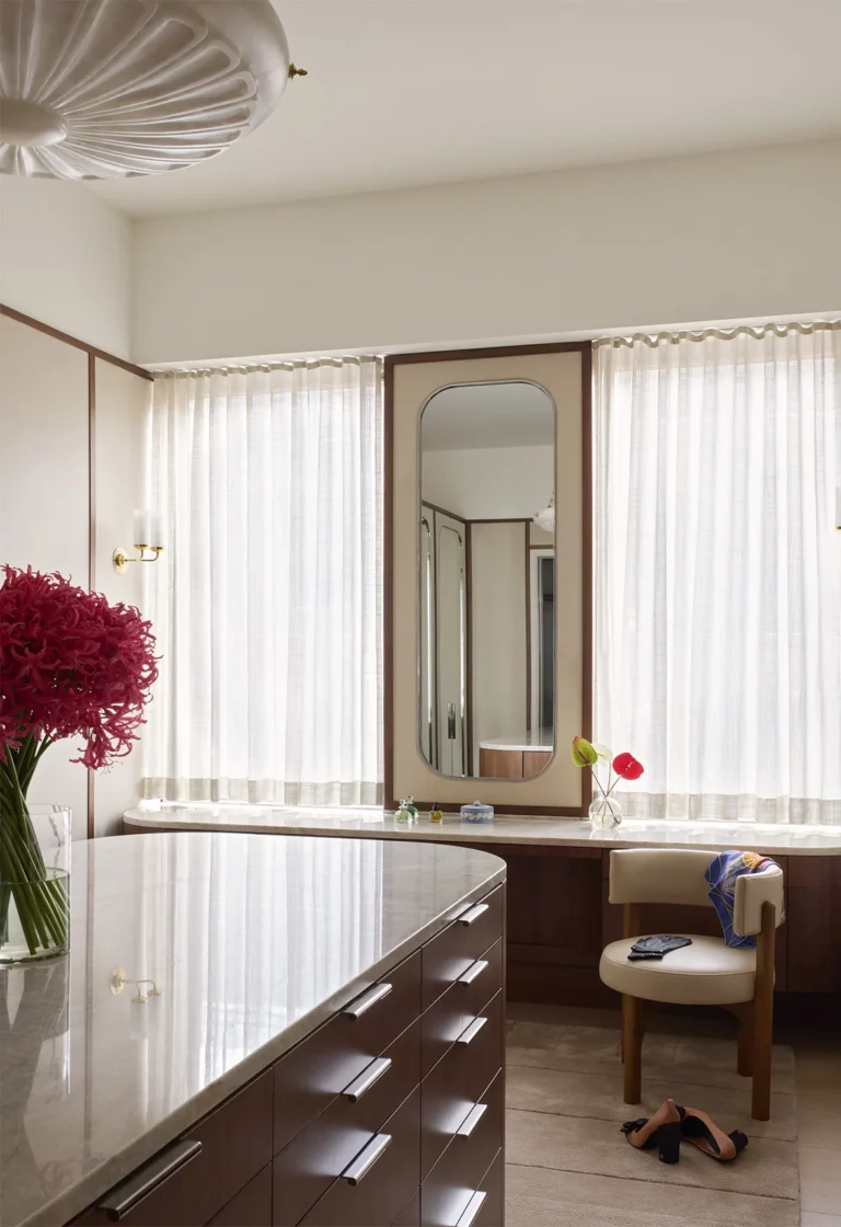 Dressing room in a Snøhetta Upper West Side residence with a custom wardrobe island, stone countertop, and a seated dressing counter framed by soft daylight.